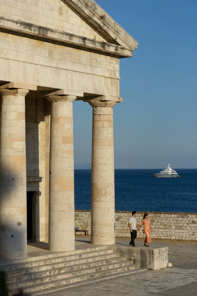 Couple holding hands as they stroll by a historical building in Greece